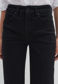 Schwarze Jeans aus Denim mit schmaler Passform. Sie verfügen über fünf Taschen, Gürtelschlaufen und einen Knopfverschluss. Der Stoff hat eine glatte Textur.