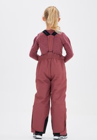 Salopettes marron avec bretelles ajustables et taille élastique. Présente des accents noirs aux chevilles et aux ouvertures latérales pour plus de facilité de mouvement.