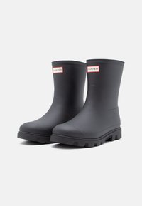 Black waterproof rubber rain boots with a mid-calf height and textured soles. Features a branded red label on the front.