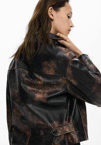 Smeđa i crna kožna jakna s mramoriranim uzorkom, skraćeni dizajn i detalji zatvaranja na gumb. Prikazana stražnja strana.