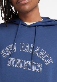 Felpa blu navy realizzata in tessuto morbido, con una grafica bianca di "NEW BALANCE ATHLETICS" in un carattere ad arco sul petto.