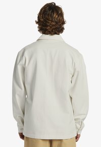 White, long-sleeve button-up shirt, relaxed fit with a fold-down collar and single button cuff detail, made of textured cotton blend fabric.
