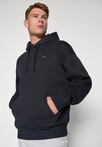 Dunkelblaues Kapuzenpullover aus weichem Stoff, mit einer Fronttasche, verstellbarem Kordelzug und gerippten Bündchen für eine komfortable Passform.