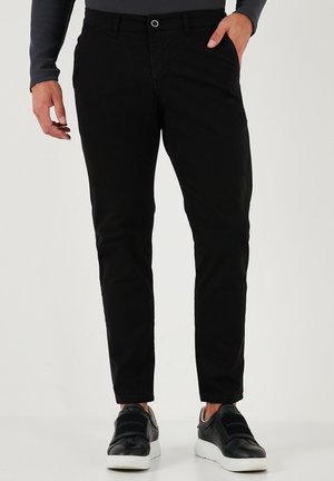 Zwarte chino's met een slim fit, gemaakt van katoen, met een knoopsluiting, riemlussen en zijzakken. Gecombineerd met zwarte sneakers.