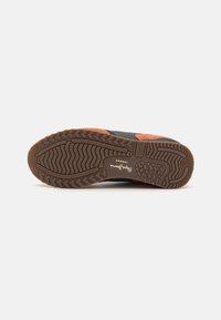 Zapatilla deportiva con una parte superior negra y acentos de gamuza naranja, que cuenta con una suela exterior de goma marrón texturizada y un patrón de perfil para tracción.