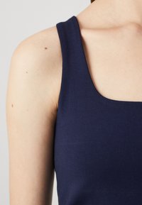 Haut sans manches bleu marine avec un décolleté carré. Tissu doux et extensible. Gros plan sur le décolleté et la zone des épaules, montrant une texture lisse.