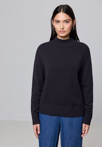Dunkelgrauer Strick-Turtleneck-Pullover mit geripptem Saum und Bündchen, kombiniert mit weiten blauen Denim-Jeans. Sanfte Textur, lässige Passform.