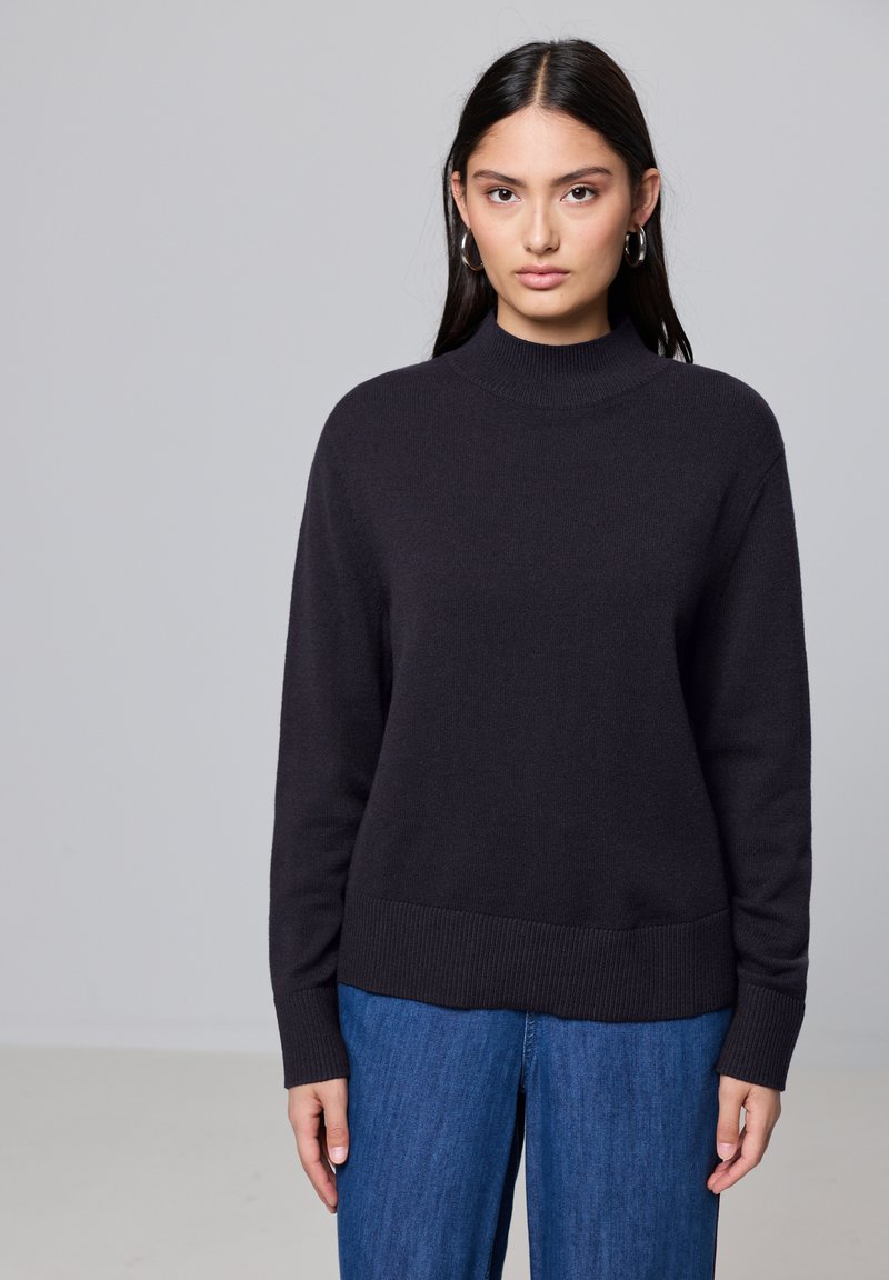 Donkergrijze gebreide coltrui, met een ribbelboord en manchetten, gecombineerd met wijde blauwe denim jeans. Soepele textuur, ontspannende pasvorm.