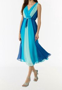 Femme portant une robe midi bleu en blocs de couleur sans manches avec une taille à cordon et des talons aiguilles bleu clair à lanières.