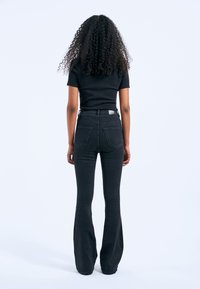 Black flared jeans with a high waist, featuring back pockets and a smooth texture. Paired with a fitted black t-shirt.