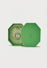 Πράσινο οκταγωνικό κουτί κοσμημάτων ανοιχτό που αποκαλύπτει κολιέ με διαμάντια, βραχιόλι και σκουλαρίκια, με το αντίστοιχο πράσινο καπάκι δίπλα του.