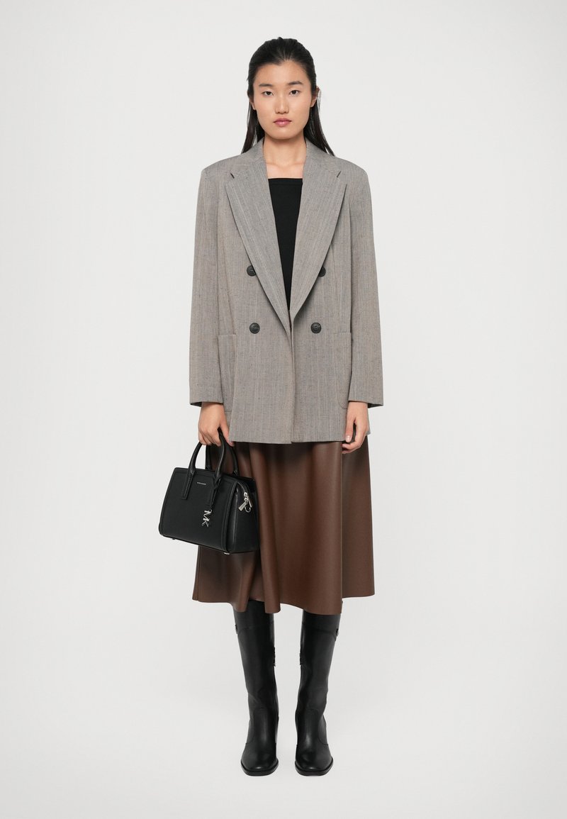 Blazer gris à double boutonnage par-dessus un haut noir, jupe marron taille haute, sac à main noir et bottes noires jusqu'aux genoux. Textures lisses et design structuré.