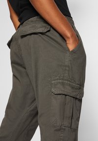 Spodnie cargo w stonowanym oliwkowym kolorze, wykonane z materiału o fakturze. Posiadają boczne kieszenie i luźny krój z elastycznym pasem.