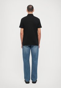 Musta polo-paita lyhyillä hihoilla, valmistettu puuvillasta, jossa on kapea malli. Yhdistetty vaaleansinisiin löysiin suoriin farkkuihin.