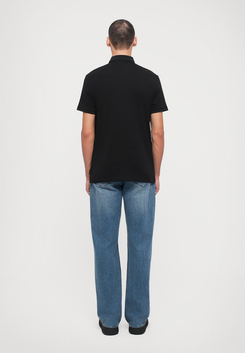 Polo noir à manches courtes, en coton, avec une coupe ajustée. Assorti à un jean droit à coupe loose bleu clair.