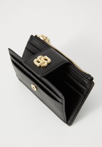 Portafoglio in pelle nera con chiusura con zip, hardware dorato e logo. Presenta diversi scomparti per carte e un bottone a pressione. Design compatto.