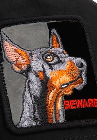 Cabeza de perro dóberman bordada de perfil con pelaje naranja y gris, junto a un texto rojo negrita que dice "CUIDADO" sobre tela negra.