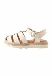 Ljusbeige sandal med flera öppna remmar, korkinsats, gummisula och en hjärtformad metallaccent på den justerbara vristremmen.