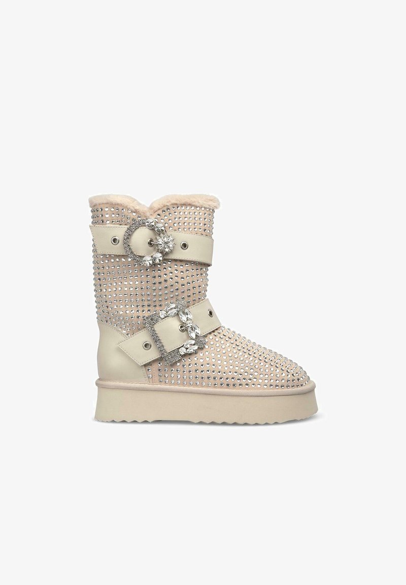 Botín beige hasta el tobillo con adornos de rhinestones, parte superior de faux fur, diseño de doble hebilla, suela esculpida y parte superior texturizada.