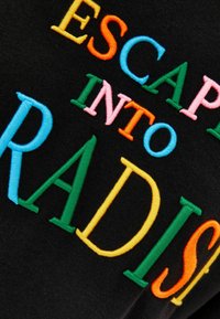 Färgglad broderad text som säger 'ESCAP INTO RADIS' på svart tyg, där varje bokstav är i en annan ljus färg.