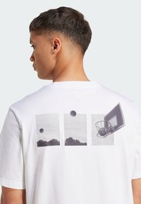 Hvid bomulds T-shirt med et grafisk print på ryggen bestående af tre paneler: en bold på himlen, landskab og en basketballkurv.