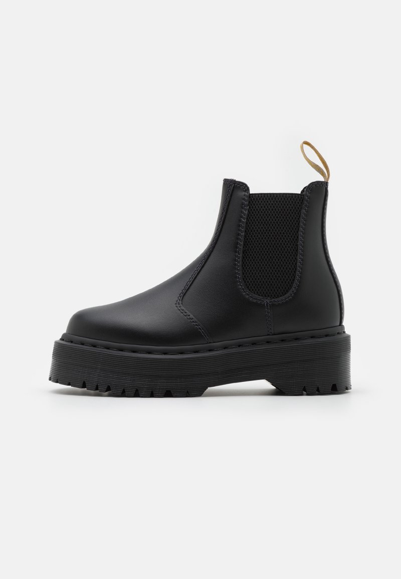 Bottine en cuir noir avec semelle épaisse à crampons, panneaux latéraux élastiques et languette beige sur fond blanc.