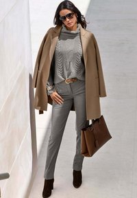 Camelkleurige jas, grijs gebreid sweater met kabelpatroon, grijze broek, bruine handtas en bruine suède enkellaarzen. Accessoires zijn grote zonnebrillen.