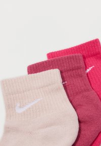 Τρία ζεύγη κάλτσες Nike σε διάφορες αποχρώσεις του ροζ: ανοιχτό μπεζ, σκούρο ροζ και φωτεινό ροζ. Κάθε ζεύγος διαθέτει το λογότυπο Nike swoosh σε λευκό χρώμα.
