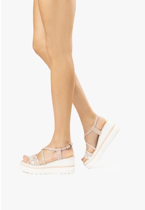 Sandali platform beige con multiple cinghie, dotati di chiusura con fibbia e un'accento testurizzato sulla parte superiore. Suola spessa bianca con una leggera curvatura.