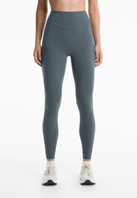 Egy tenger zöld színű, magas derekú leggings, rugalmas anyagból készült, sima textúrával, látható minták vagy varrások nélkül.