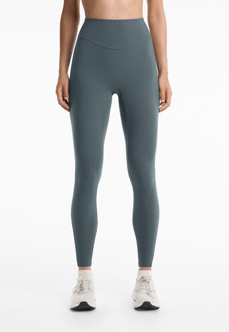 Egy tenger zöld színű, magas derekú leggings, rugalmas anyagból készült, sima textúrával, látható minták vagy varrások nélkül.