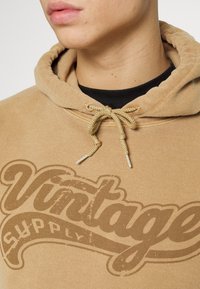Vintage Supply UNISEX HOODIE WITH VINTAGE SUPPLY RETRO VARSITY LOGO GRAPHIC - Camisola - tan