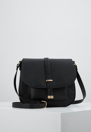 Sort tekstureret læder crossbody taske med klap, guldfarvet spænde og justerbar skulderrem på hvid overflade.