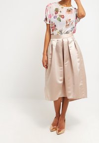 Hvězdicový top s krátkými rukávy, kombinovaný s plisovanou saténovou sukní po kolena v světle růžové barvě, doplněný o béžové lodičky se špičatou špičkou.