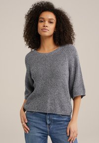 Grå stickad tröja med rund halsringning, korta ärmar och ett strukturerat mönster. I kombination med blå denimjeans.