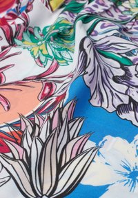 Ein floraler Stoff in lebendigen Farben zeigt detaillierte botanische Drucke auf einem weißen und blauen Hintergrund, mit einer glatten, leichten Textur.