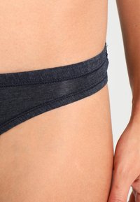 Marineblauwe katoenmix bikini met een soepele tailleband, naaddetails en een minimalistisch ontwerp, waarbij een close-up van de zijaanzicht wordt getoond.