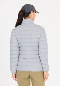 Lys grå pufferjakke med quiltet design, høj krave og lange ærmer. Kombineret med khaki-bukser og en mørk kasket. Glat tekstur.