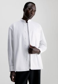 Witte lange mouwen shirt met een Mandarin kraag, sluiting met knopen aan de voorkant, enkele borstzak en een relaxte pasvorm. Glad katoenmateriaal.