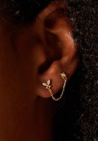 Boucles d'oreilles en or ornées de deux accents en pierres précieuses, dont un avec une taille marquise, reliés par une délicate chaîne. Gros plan de l'oreille et de la boucle d'oreille.