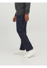 Marinblå byxor i bomullsblandat tyg med rak benform. Kombineras med vita sneakers och en mörkgrå tröja.