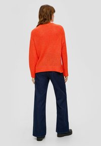 Helderoranje gebreide trui met een ontspannen pasvorm, geribde onderrand en lange mouwen, gecombineerd met donkerblauwe wijde jeans en zwarte platform schoenen.
