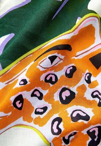 Kleurvolle stof met een gedurfd oranje en zwart luipaardpatroon, aanvulled met groene en paarse accenten op een witte achtergrond; zachte, gestructureerde stof.