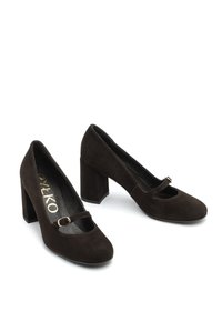 Temno rjave semiš čevlje na visoki peti z zaobljenim nosom, naramnicom s srednjo debelim trakom z majhnim zlatim sponko ter debelim kvadratnim peto.