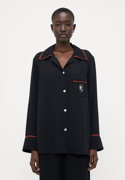 Schwarzes Schlafshirt mit roter Einfassung, Knopfleiste und einer Brusttasche mit Logo. Lange Ärmel mit ausgestellten Manschetten. Weicher Stoff.