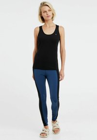Top sportivo nero con design aderente, abbinato a leggings blu e neri con pannelli laterali. Tessuto liscio e materiale leggero.