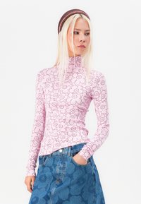 Maglione a maniche lunghe con colletto alto in rosa chiaro con motivo floreale nero. Abbinato a una gonna di jeans blu, con cuciture visibili e tasche.