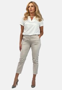 Biała bluzka z krótkim rękawem i dekoltem w kształcie litery V, zestawiona z jasnobeżowymi spodniami typu slim fit i wielokolorowymi szpilkami, bez wzorów ani ozdób.