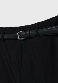 Schwarze Hosen mit glatter Textur, ausgestattet mit einem schwarzen Leder-Gürtel und einer silbernen Metallschnalle. Schlichtes Design ohne sichtbare Muster.