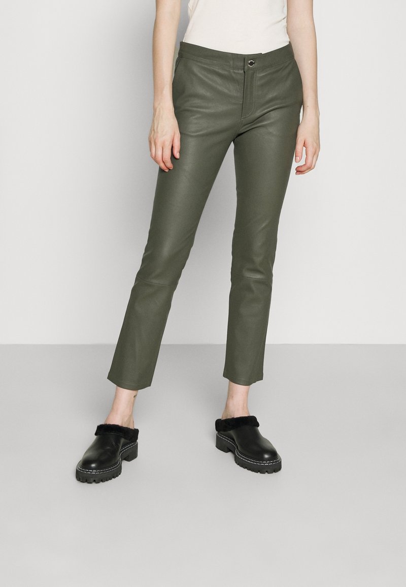 Olijfgroene nep leren broek met een slim fit, voorzien van een sluiting aan de voorkant en een enkel lengte, gecombineerd met zwarte zachte muiltjes.